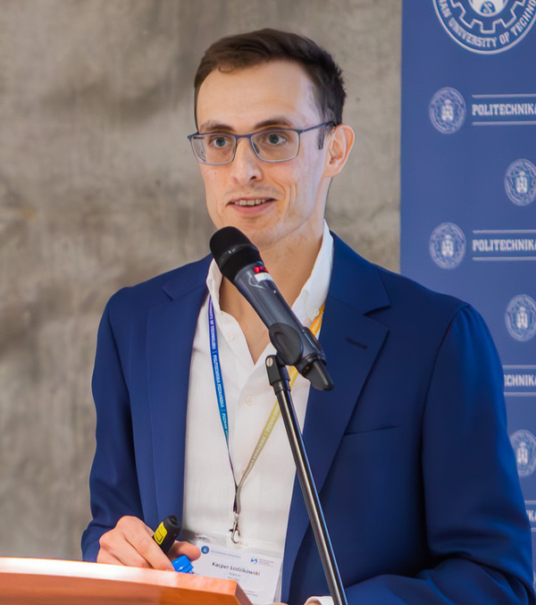 Kacper Łodzikowski in a blue suit speaking into a microphone at a podium